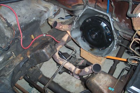 1978 Ford Bronco - A close-up view of a vehicle's engine bay, focusing on the transmission housing and torque converter. The area shows significant rust and g…