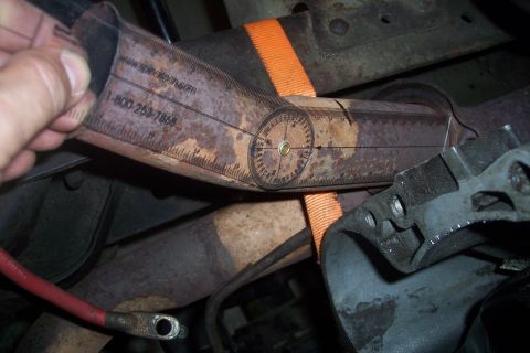 1978 Ford Bronco - A close-up shows a protractor tool being used to measure the angle of a rusty exhaust pipe. The tool has markings for degrees and a website…
