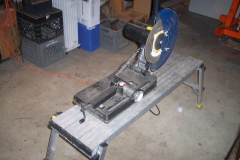 1978 Ford Bronco - A metal chop saw is mounted on a portable metal workbench. The saw has a blue safety guard and a cutting disc. The workbench is set up on a…