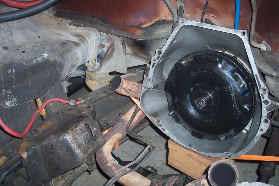 Torque converter inside transmission bell housing, rusty exhaust pipes, engine bay components, wiring.