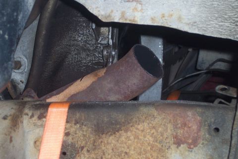 1978 Ford Bronco - A rusty exhaust pipe is visible under a vehicle, with a bright orange strap securing a metal component in the foreground.