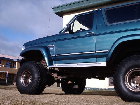 1996 Ford Bronco - This teal Ford Bronco features a lifted suspension and off-road tires, parked on a grassy area.