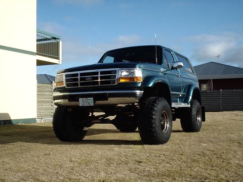 1996 Ford Bronco - A lifted 1996 Ford Bronco with oversized tires sits on a grassy lawn under a blue sky.