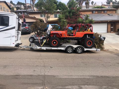 1992 Jeep Wrangler - An orange Jeep CJ-7 is loaded onto a trailer, accompanied by a toy Jeep and an RV.
