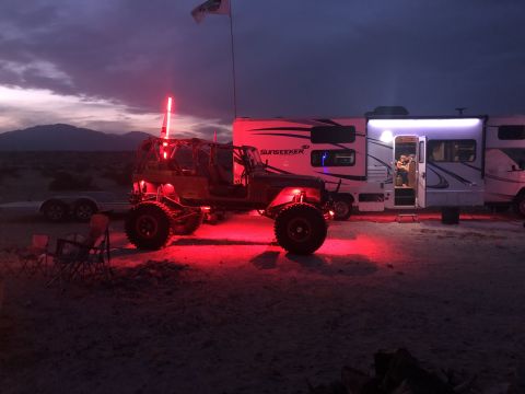 1992 Jeep Wrangler - A heavily modified Jeep Wrangler is illuminated by red lights next to a recreational vehicle in a desert landscape.