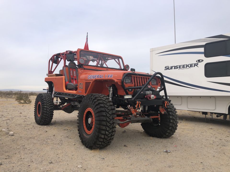 Orange 1992 Jeep Wrangler with roll cage and large tires parked next to an RV