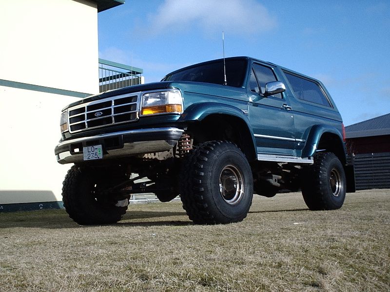 Lifted teal Ford Bronco on big mud tires, front 3/4 view on grass