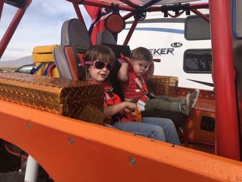 1992 Jeep Wrangler - Two children sit inside an orange off-road vehicle, with a large RV visible in the background.