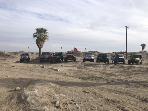 1992 Jeep Wrangler - A group of off-road vehicles, including several Jeep Wranglers, are parked in a desert area under a cloudy sky.