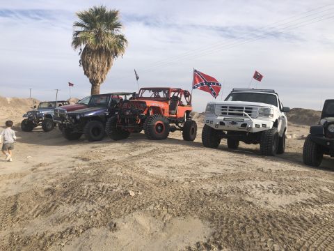 1992 Jeep Wrangler - A group of customized off-road vehicles are gathered in a desert landscape under a cloudy sky.