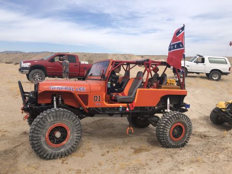 1992 Jeep Wrangler - An orange Jeep CJ-7, modified for off-roading, is parked in a desert landscape with other vehicles.