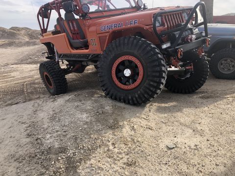 1992 Jeep Wrangler - This heavily modified Jeep Wrangler sits on a sandy, uneven surface with another vehicle partially visible to the right.