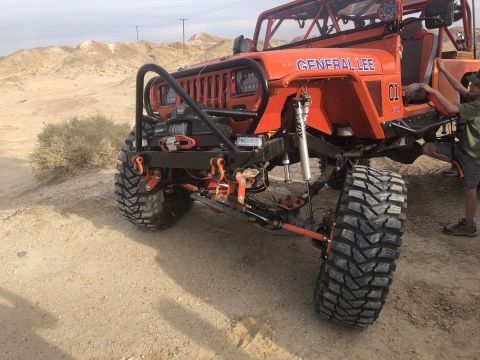 1992 Jeep Wrangler - An orange Jeep Wrangler modified for off-roading is parked in a desert landscape.