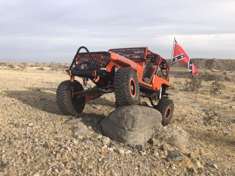 1992 Jeep Wrangler - Modified Jeep with large tires and a roll cage navigates rocky terrain, flying a confederate flag.