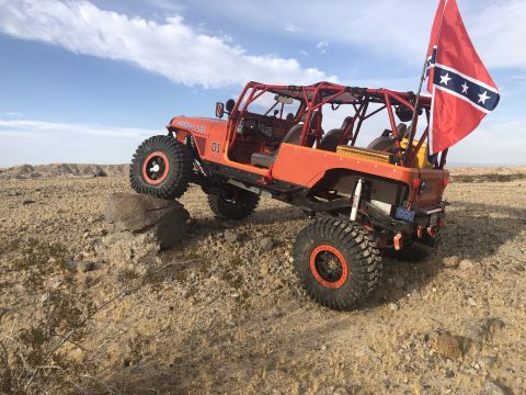 1992 Jeep Wrangler - This heavily modified off-road vehicle is navigating rocky terrain under a partly cloudy sky.