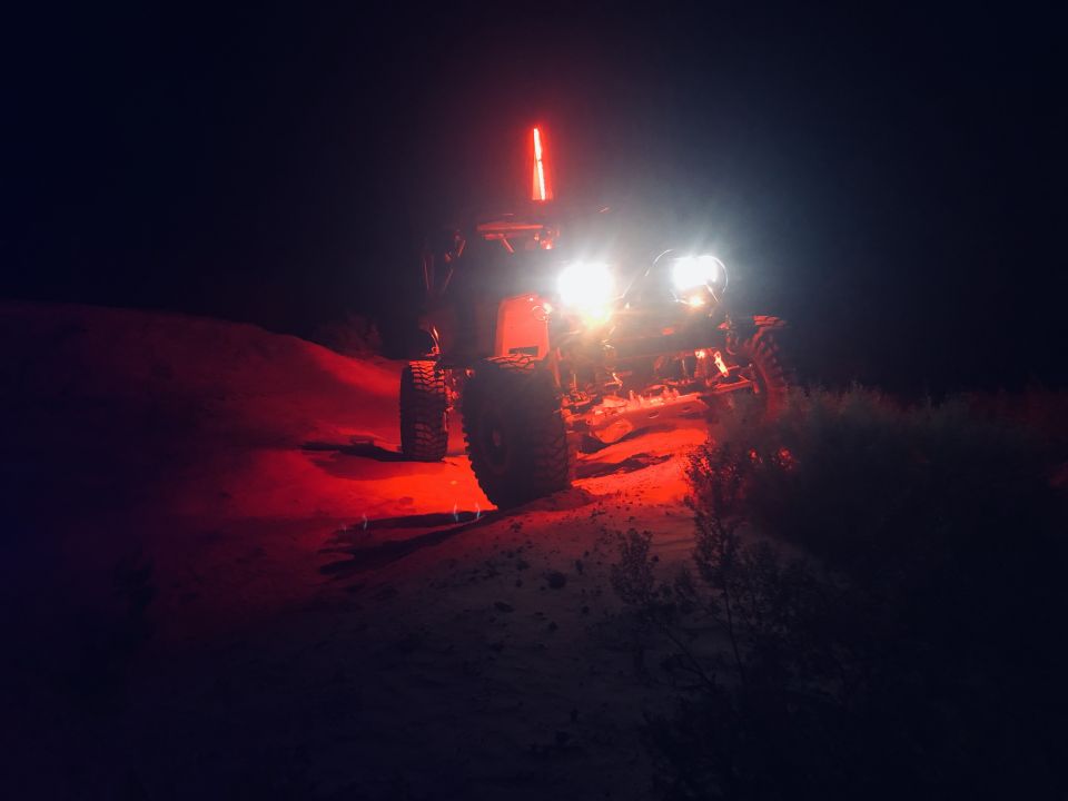 Off-road buggy with bright headlights and a red light bar, driving on a dirt hill at night