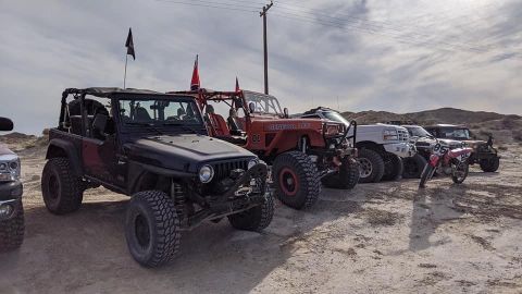 1992 Jeep Wrangler - Several off-road vehicles, including a black Jeep Wrangler, are parked in a desert landscape under a cloudy sky.