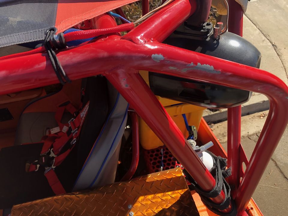 Close-up of a red roll cage inside an off-road vehicle, showing a racing seat and harness