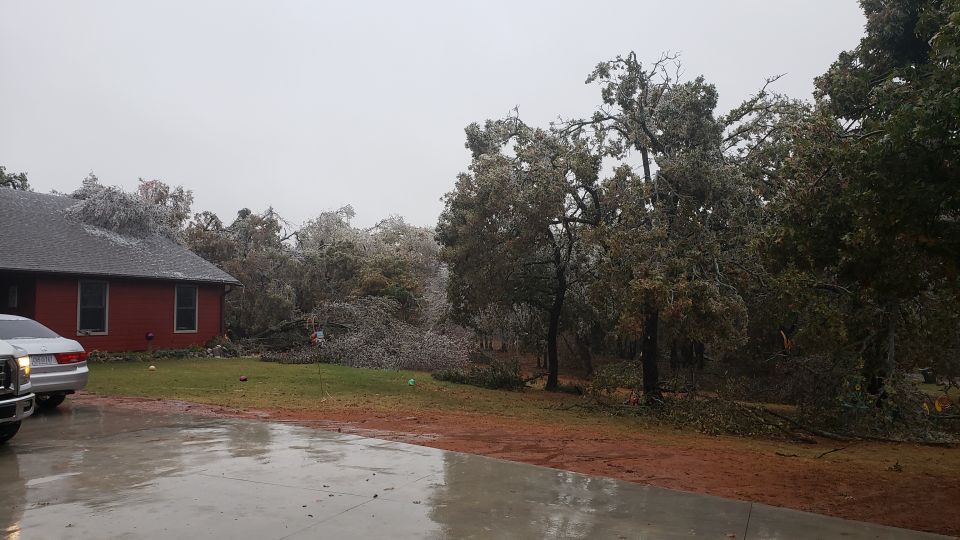White pickup truck parked in front of a red house with ice-covered trees and debris