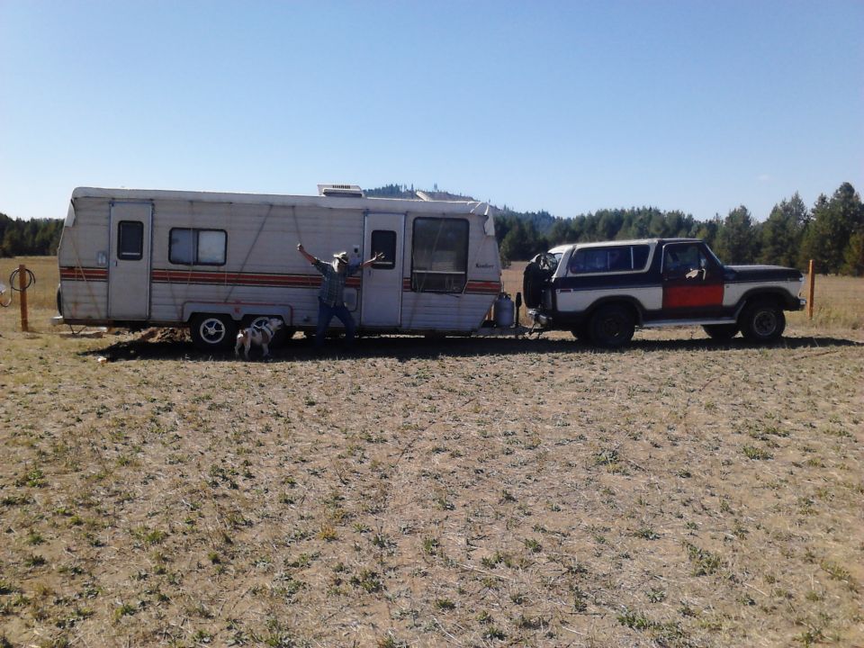 1978 Ford Bronco towing a travel trailer in a dry, grassy field