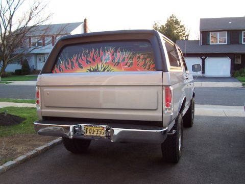1990 Ford Bronco - Rear view of a silver Ford Bronco with a flame decal on the back window and a chrome bumper.