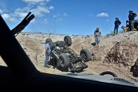 1992 Jeep Wrangler - An off-road Jeep Wrangler is flipped on its side in a dirt ditch, with several people and a dog observing the scene.