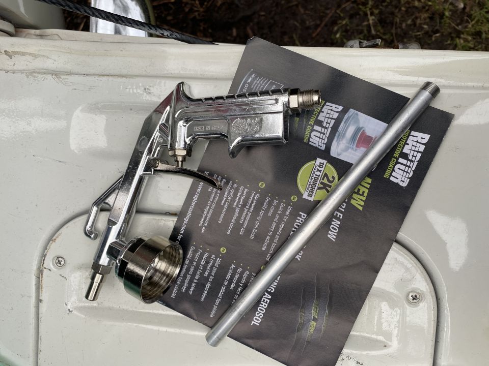 Chrome spray gun and metal tube on Raptor Protective Coating document on a white vehicle surface.