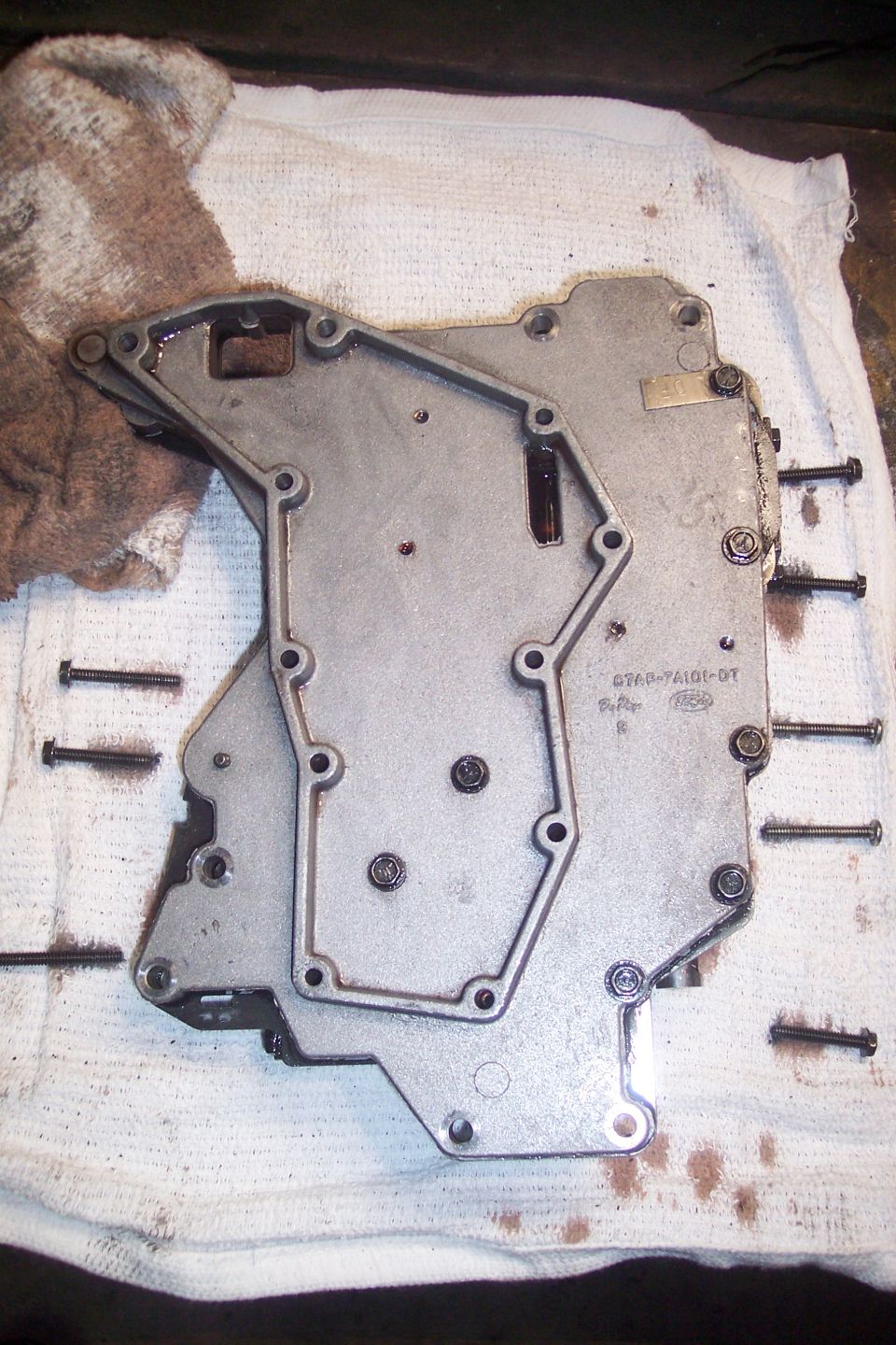 Disassembled automatic transmission valve body with bolts on a white cloth.