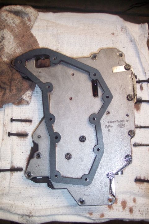 1973 Ford F-250 - A transmission valve body with a gasket is laid out on a white towel next to a stained brown rag. Several screws are also visible on the to…