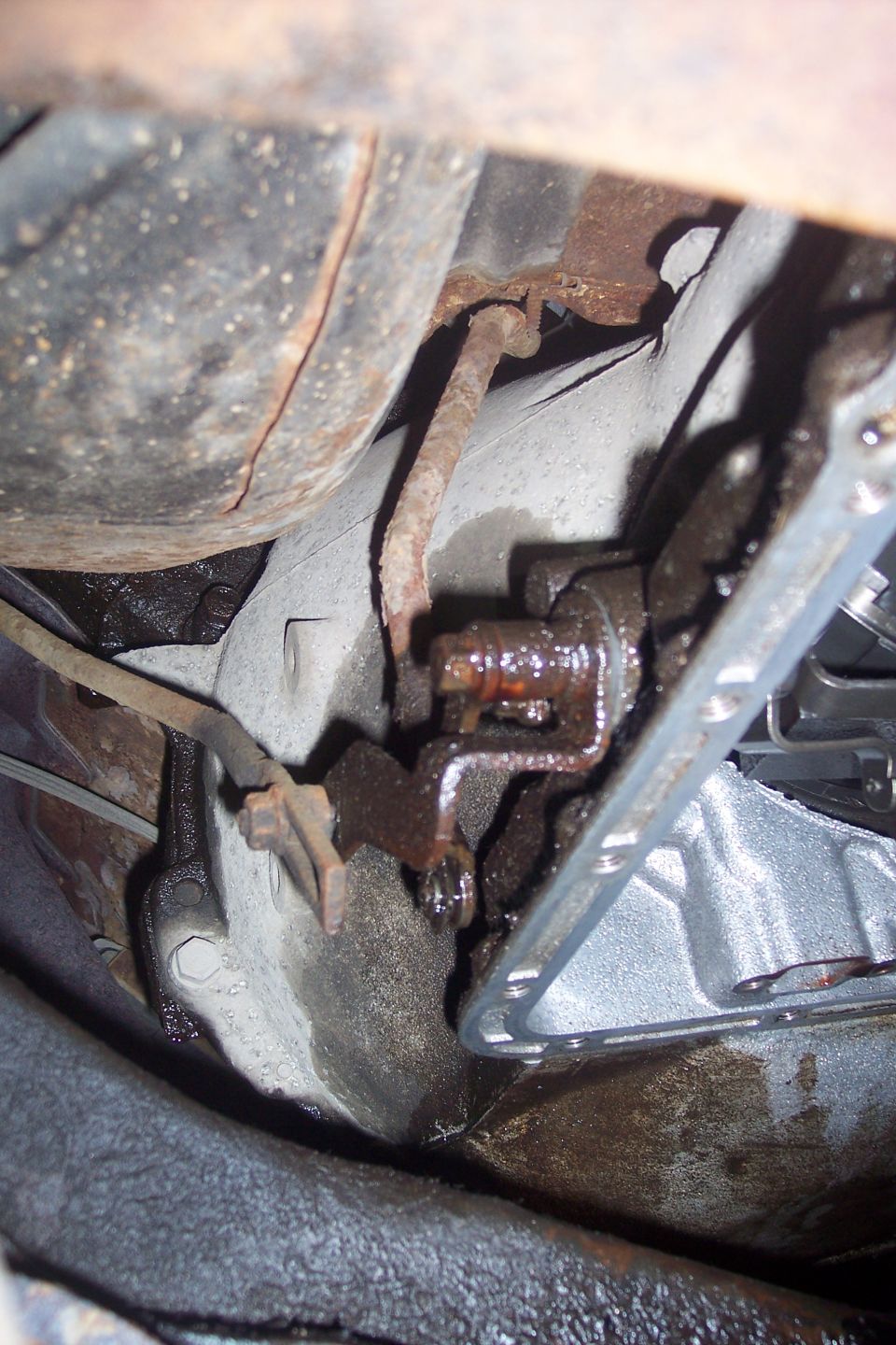 Underside of a vehicle showing rusted transmission parts and oily residue.