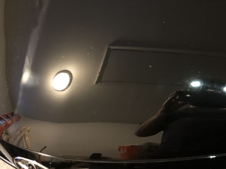 Reflection of a person holding a phone on a glossy black car hood.