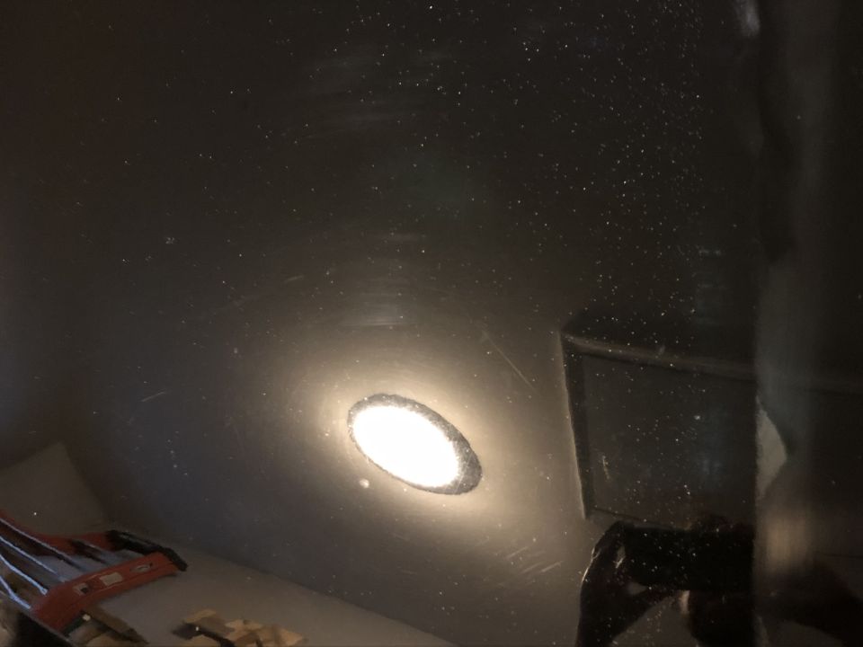 Interior of a vehicle with a light on, showing a dark, speckled surface and a tool.
