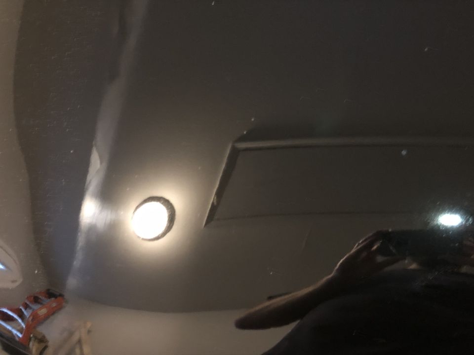 Reflection of a person with a camera on a dark, reflective vehicle surface with a light.