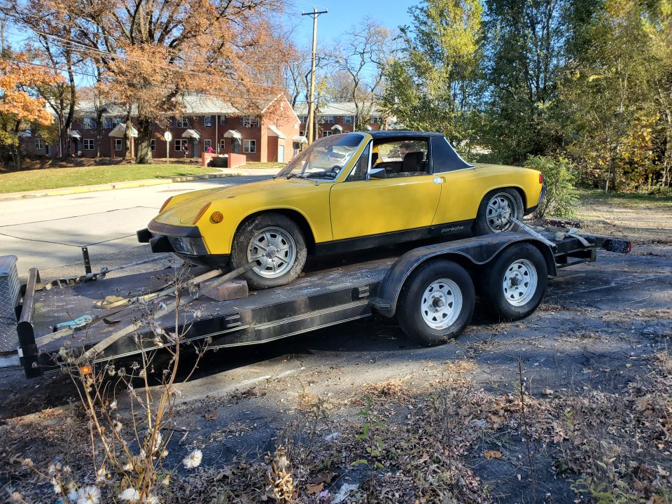 Yellow Porsche 914 loaded on a tandem-axle car trailer in a parking lot