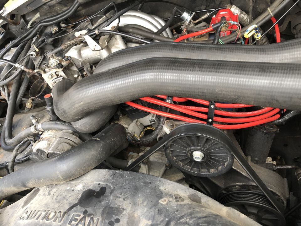 Engine bay of a 1989 Ford Bronco, showing distributor, spark plug wires, hoses, and belts.