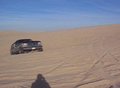 1989 Ford Bronco - A 1989 Ford Bronco navigates sandy terrain under a clear blue sky.