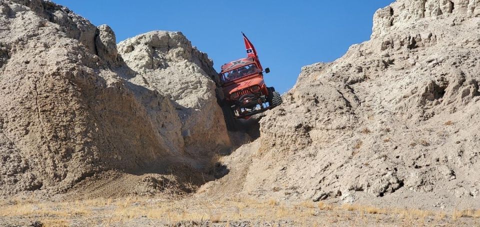 Red Jeep Wrangler climbing a steep dirt path between rocky hills.