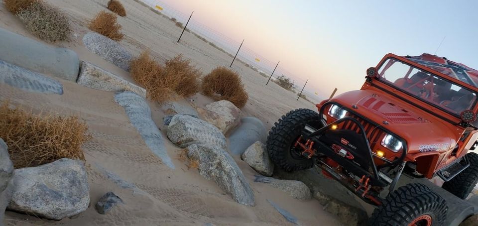 Orange off-road Jeep Wrangler climbing a sandy hill with large tires and custom bumper.