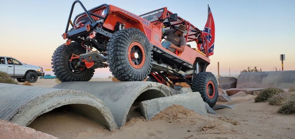 Orange Jeep Wrangler "General Lee" off-roading over concrete pipes with a Confederate flag.