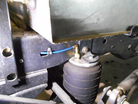 1992 Ford Bronco - A close-up view shows a blue air line connected to a brass fitting on an air suspension bag mounted to the frame of a vehicle.