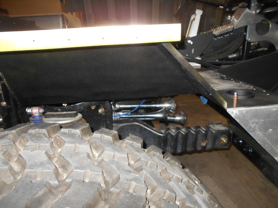 Close-up of vehicle suspension, tire, and air horns.
