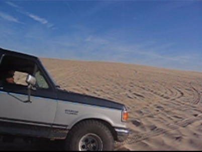1989 Ford Bronco - Ford Bronco navigates sandy terrain, leaving tire tracks on the dunes.