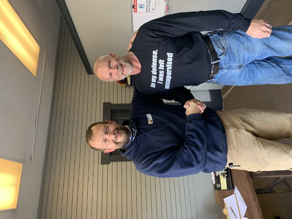 Two men shaking hands, one wearing a shirt that says "In my defense, I was left unsupervised".
