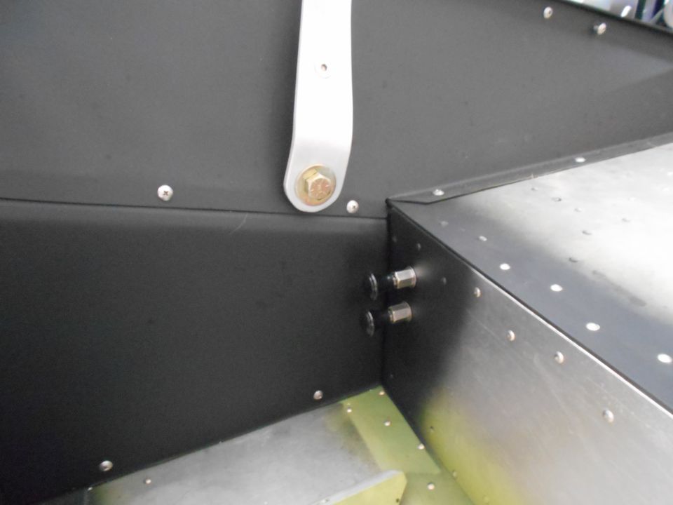 Interior corner of a vehicle with black panels, rivets, bolts, and a silver bracket.