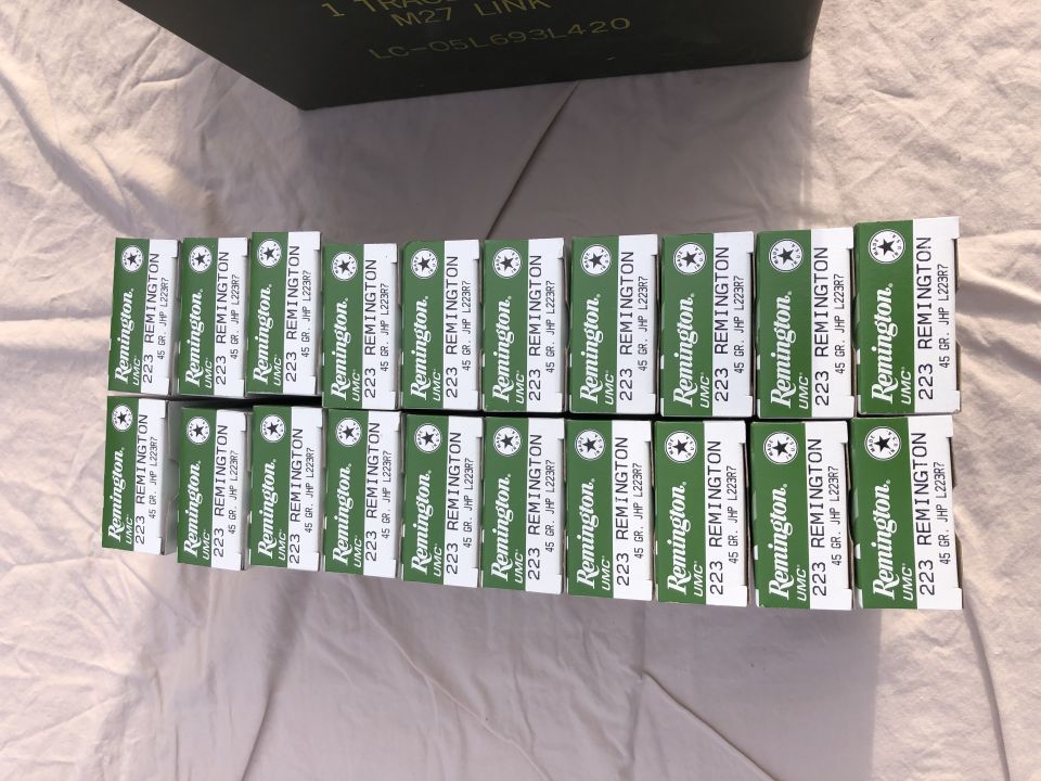 Rows of green Remington 223 ammunition boxes on a white cloth surface, with a dark green ammo can in the background