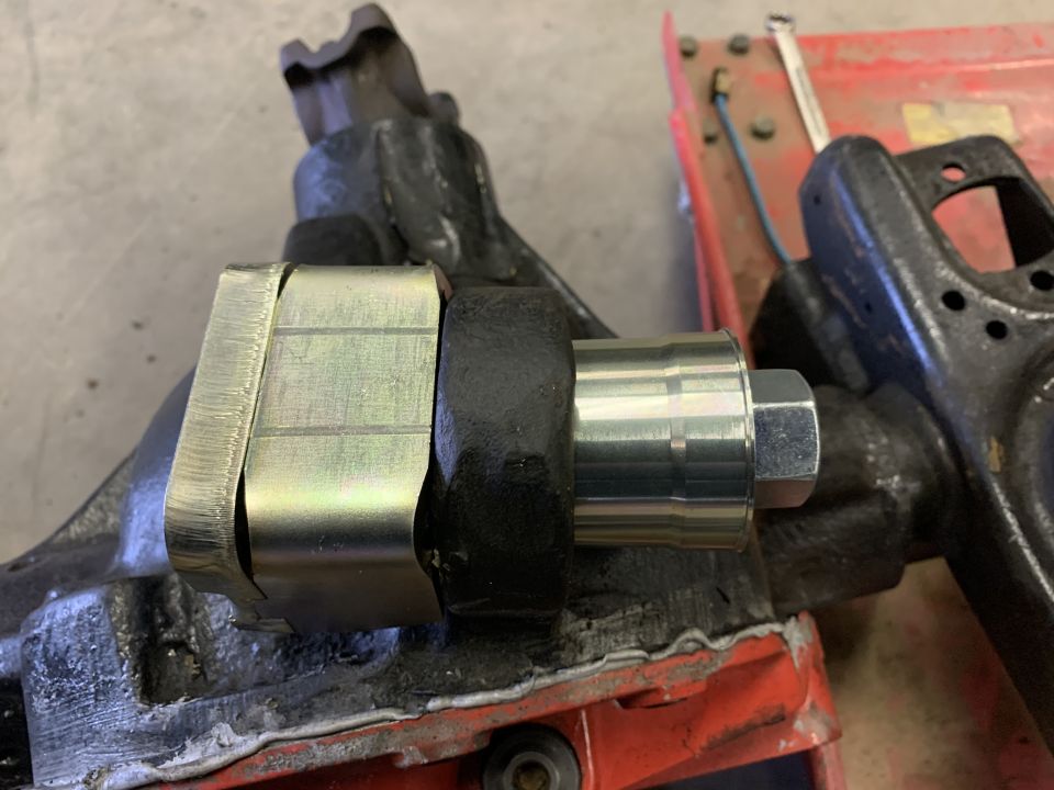 Close-up of a metal part with a bolt and nut, possibly a suspension component, on a workbench