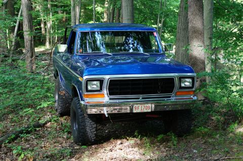 1979 Ford Bronco - Blue 1979 Ford Bronco with off-road tires sits in a forest clearing.