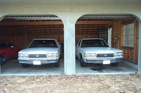 1991 Ford Crown Victoria LTD - Two white Ford Crown Victorias are parked side-by-side in a garage, viewed from the front.