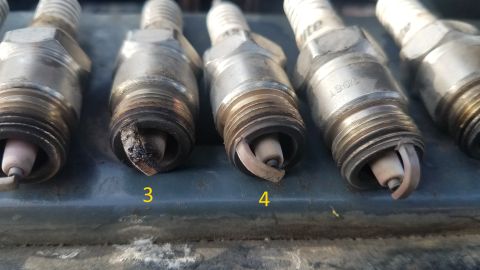 1985 Ford Bronco - Close-up view of four spark plugs, two of which are labeled with numbers 3 and 4, showing varying degrees of wear and carbon fouling.
