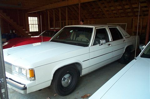 1991 Ford Crown Victoria LTD - A white sedan is parked in a garage with other vehicles.